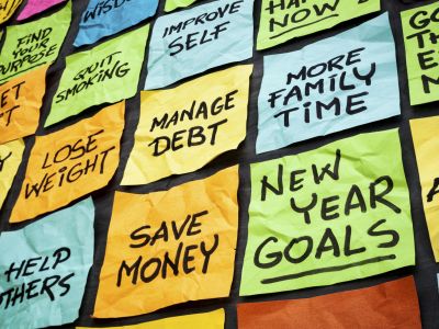 a wall of sticky notes with New Year goals - or resolutions - handwritten on them including save money, manage debt, more family time, get fit, lose weight, find purpose.