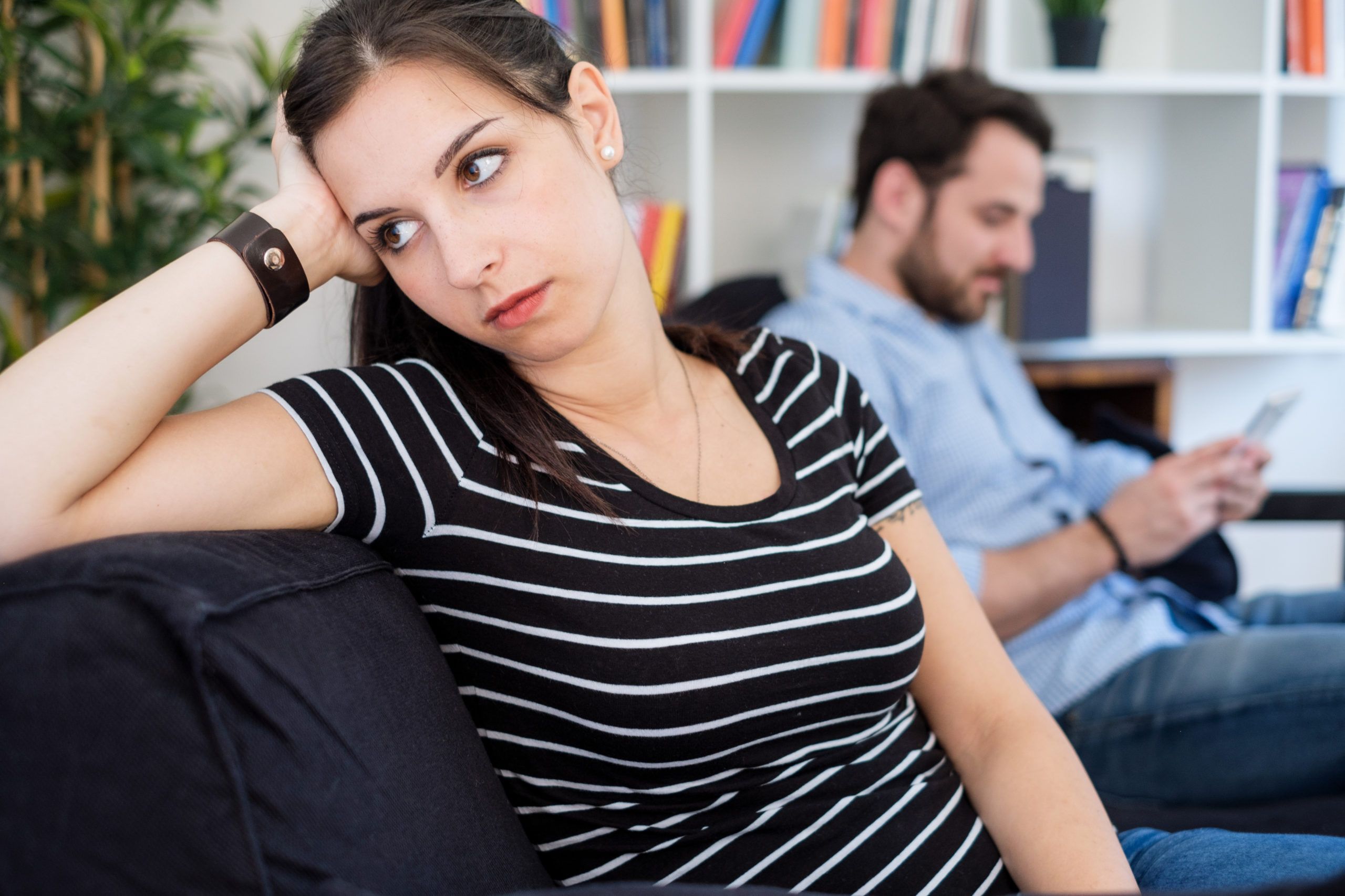 a man and woman sitting together, she'd bored and he's looking at his phone.