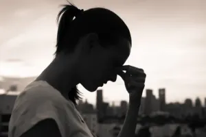 Woman in profile, with head bowed, holding her forehead as though it hurts. The image is dark, hinting at depression.