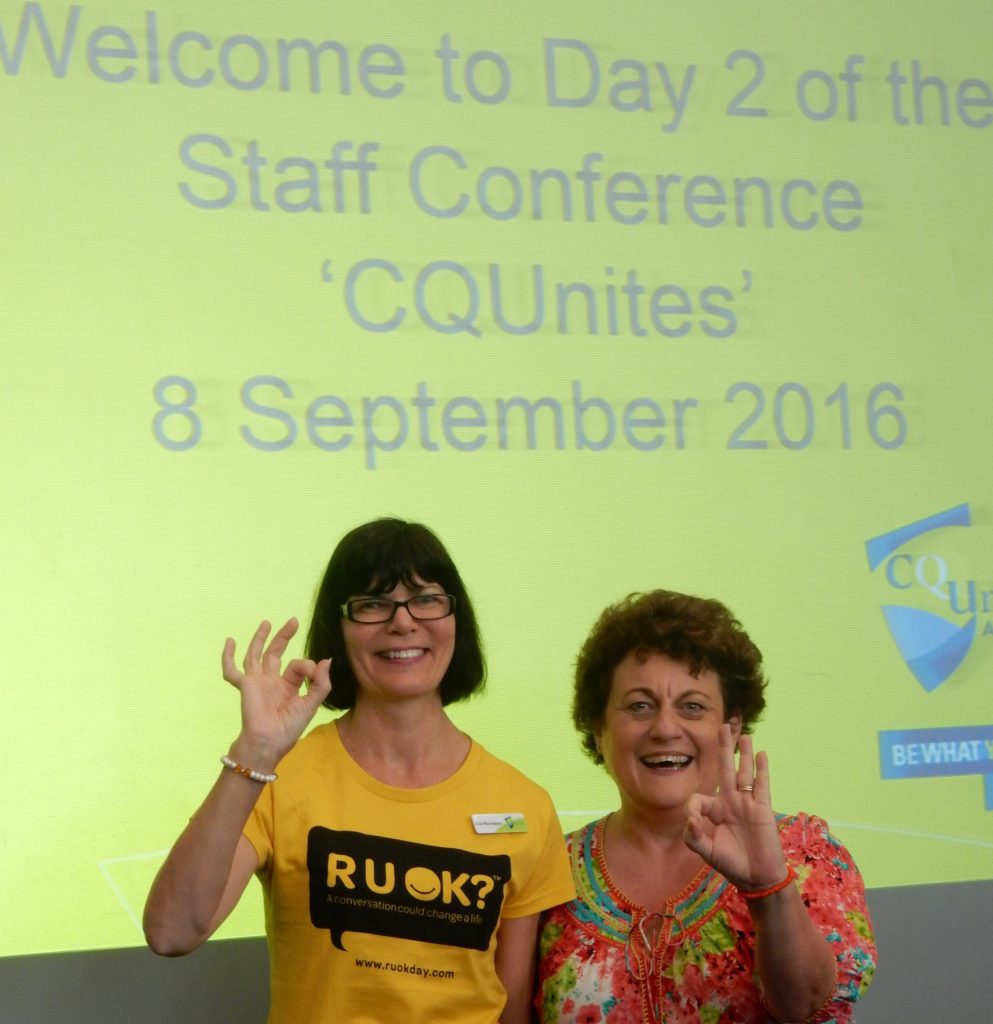 Heather Joy and a lady wearing an R U OK tshirt standing in front of a projected image for a conference