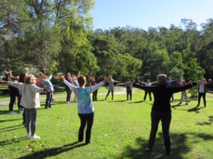 a circle of 20 people arms outstretched laughing in a park