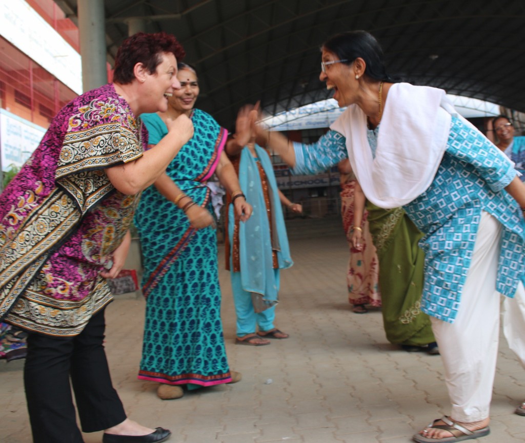 women doing laughter yoga, face one another, bending at waist and laughing