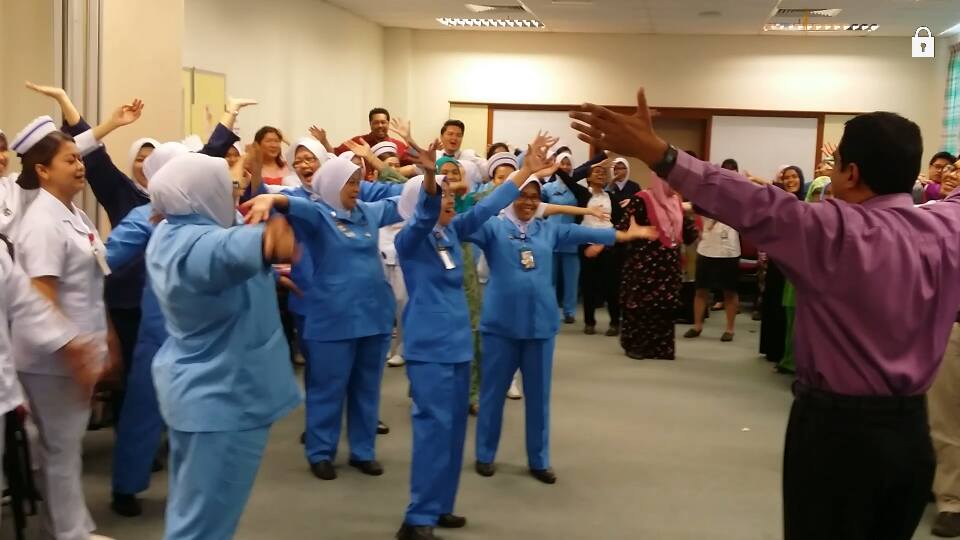 Hosiptal staff are in a training session, arms outstretched and laughing, with Dr Arul Kumaran.