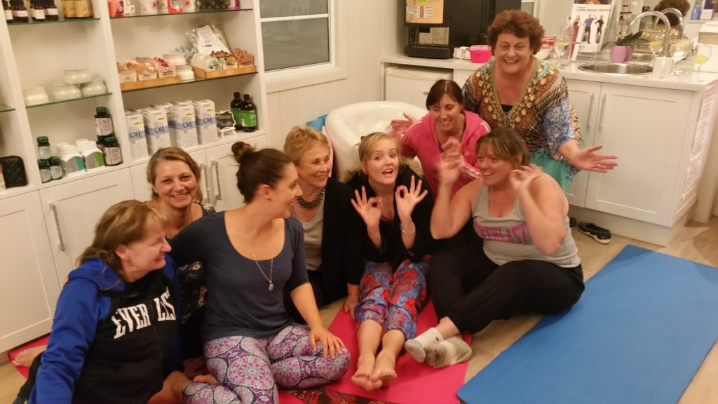 A group of women in a wellness studio sitting on yoga mats, girl in the middle making the okay symbol with her fingers