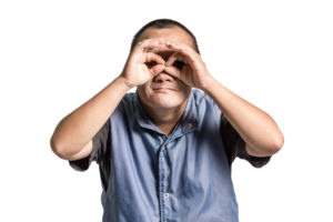 A man with Downs sydrome holds his hands to his eyes as though looking through glasses.
