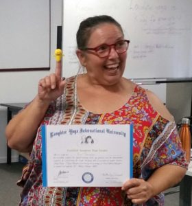 A woman smiles as she holds her laughter yoga leader certificate