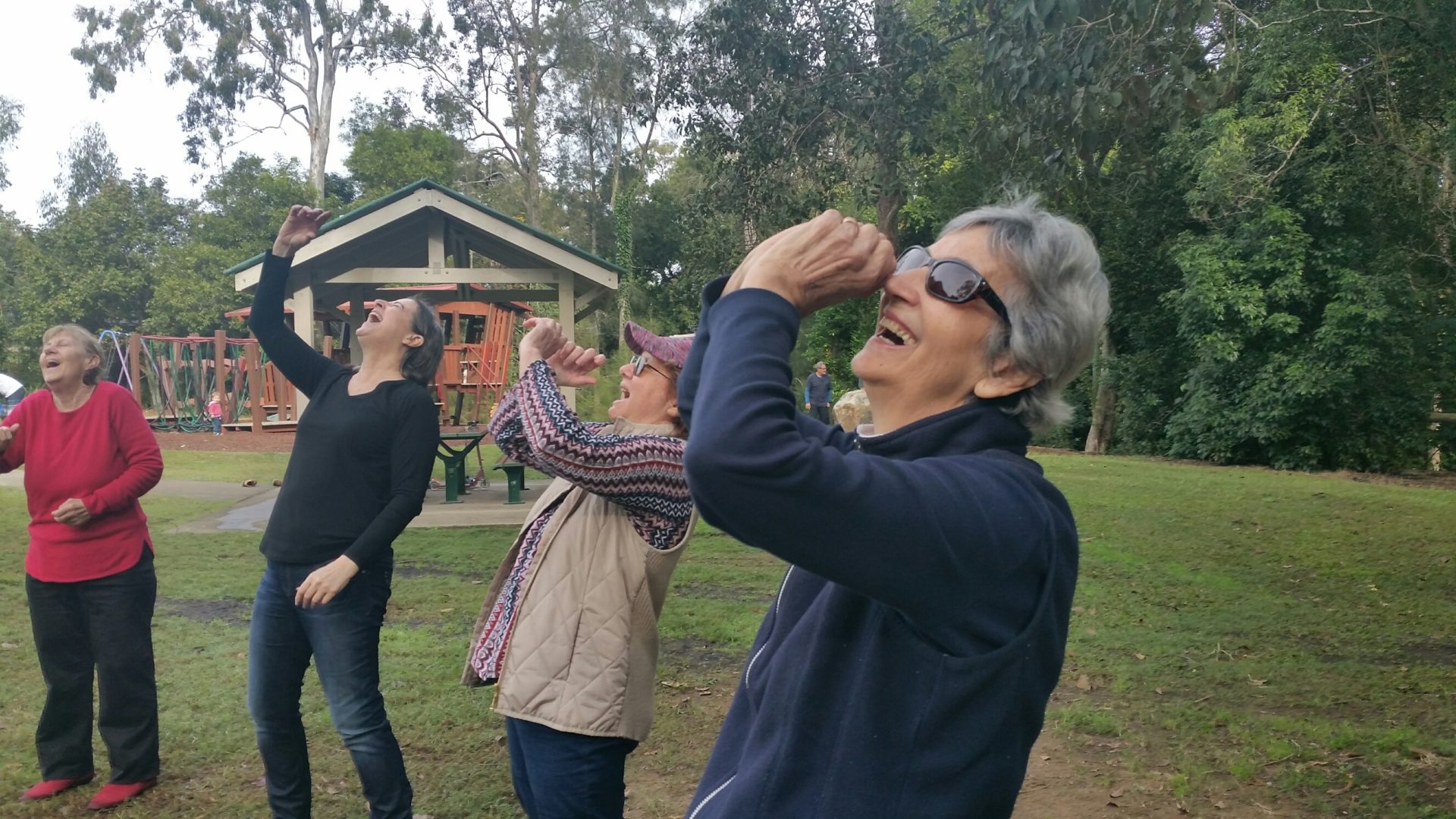 Older people in park laughing as part of laughter yoga session