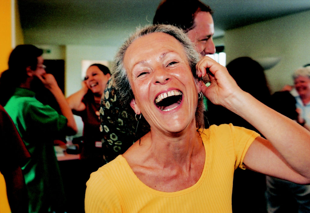 Lady laughing at a workplace wellness session with other people all with one hand on their ear