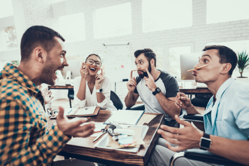 Group of office workers sit around a table pulling faces, having fun, during a meeting break