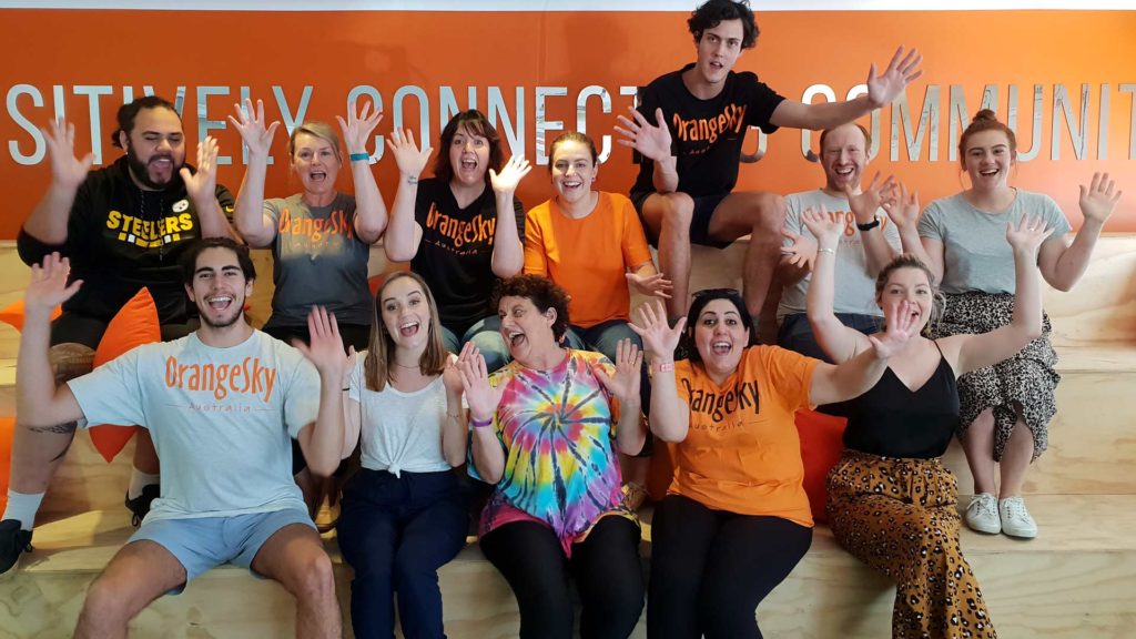 workplace wellbeing program showing group of young men and women smiling with hands up wearing OrangeSky tshirts