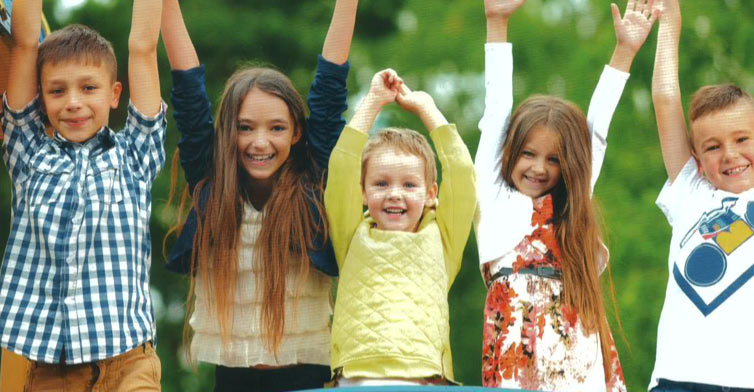 Five children standing in a row smiling with hands in the air