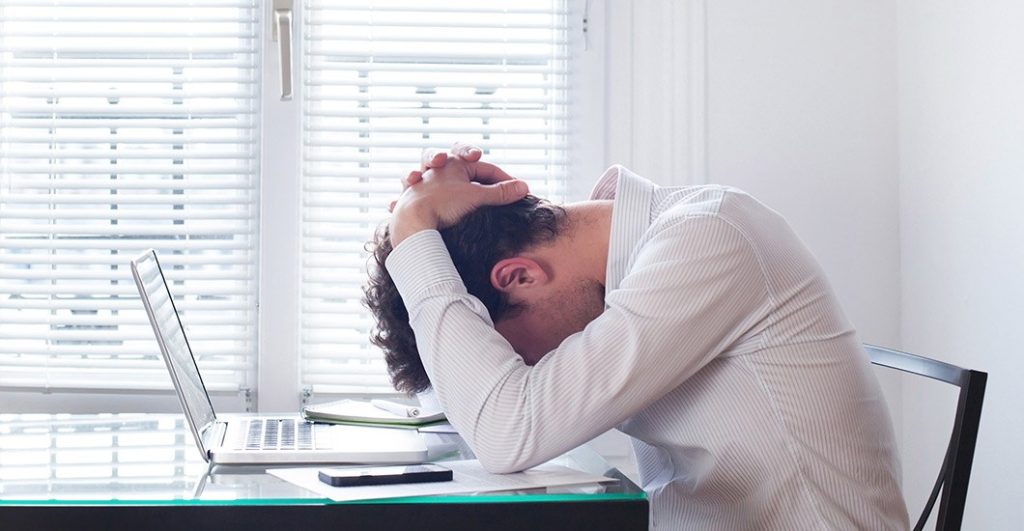 Man sitting in front of laptop with hands on his head looking stressed