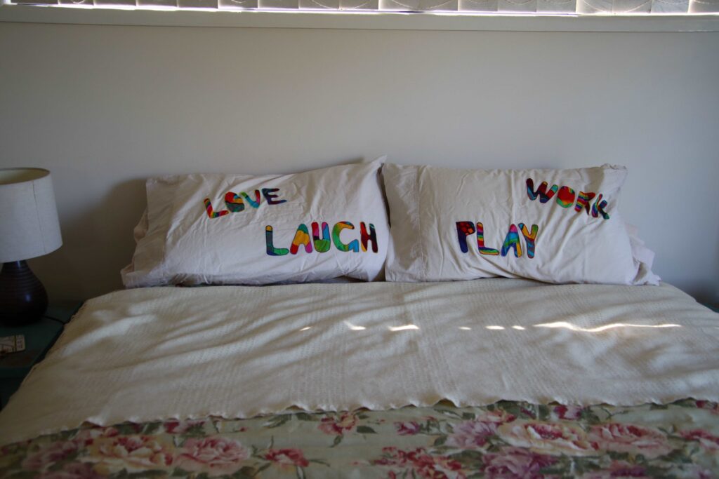 A bed made, with pillows that have the words laugh love play and work