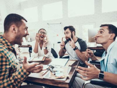 Group of office workers sit around a table pulling faces, having fun, during a meeting break