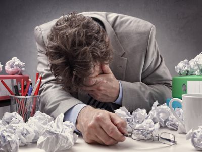 Overworked, depressed and exhausted office workers at his desk surrounded by a pile of work