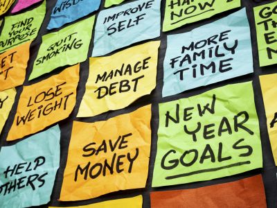 a wall of sticky notes with New Year goals - or resolutions - handwritten on them including save money, manage debt, more family time, get fit, lose weight, find purpose.