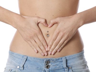 A woman wearing low, on the hip jeans, places her hands on her abdomen to form a heart shape round her navel