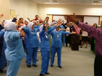 Hosiptal staff are in a training session, arms outstretched and laughing, with Dr Arul Kumaran.