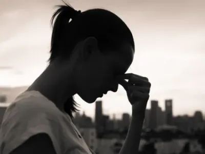 Woman in profile, with head bowed, holding her forehead as though it hurts. The image is dark, hinting at depression.