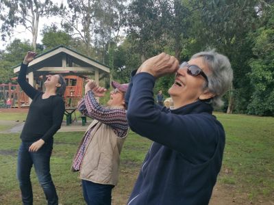 Older people in park laughing as part of laughter yoga session