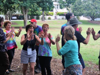 Group of people in a park practising laughetr yoga, hand clapping and laughing