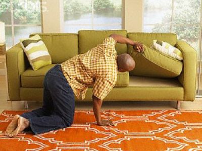man on his knees, looking under a couch seat for something he has lost